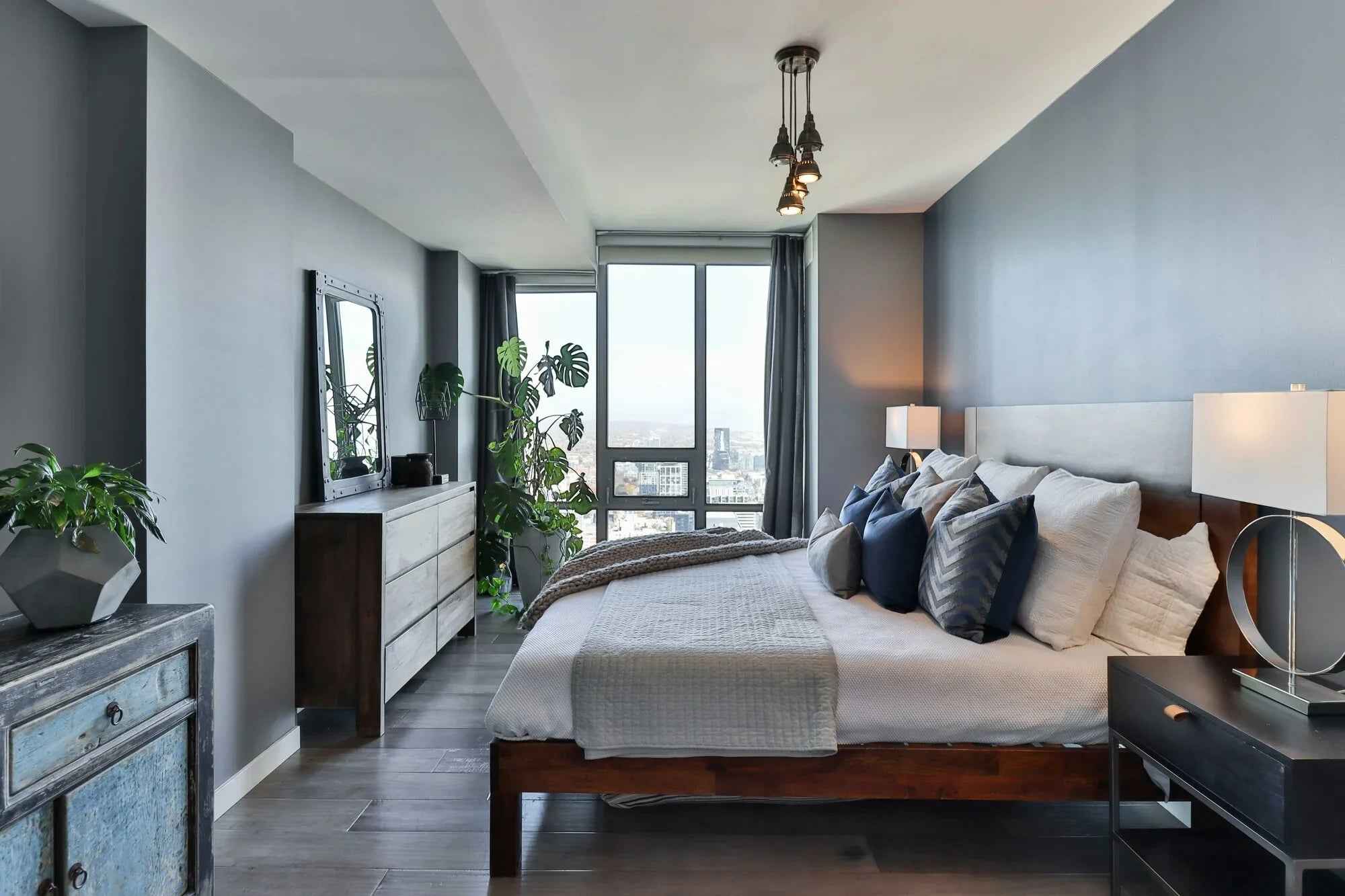 Modern bedroom with wooden bed, gray walls, city view window, and decorative plants